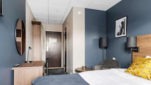 Habitación de hotel con una cama, un escritorio, una silla, una mesa redonda, una lámpara y un espejo.