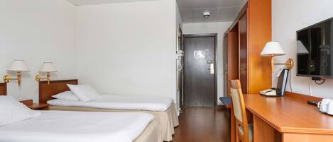 Habitación de hotel con dos camas individuales, un escritorio con silla, un televisor y una lámpara de escritorio.
