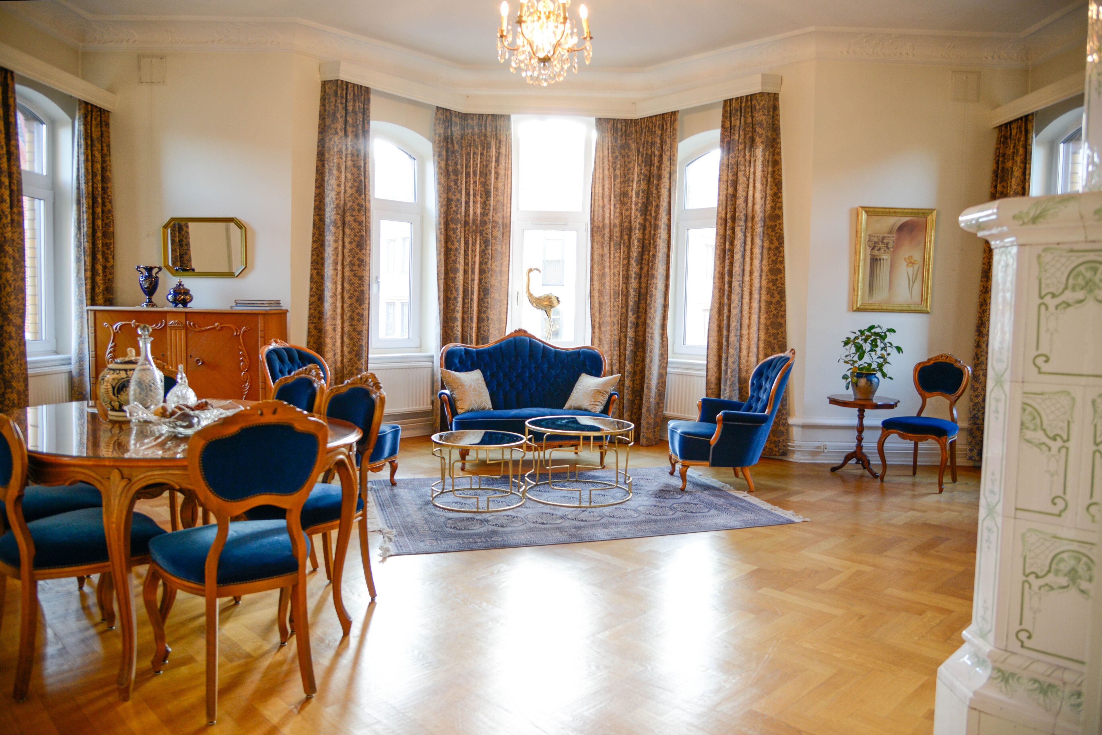 Een ruime kamer met een eethoek, een blauwe bank en een kroonluchter.
