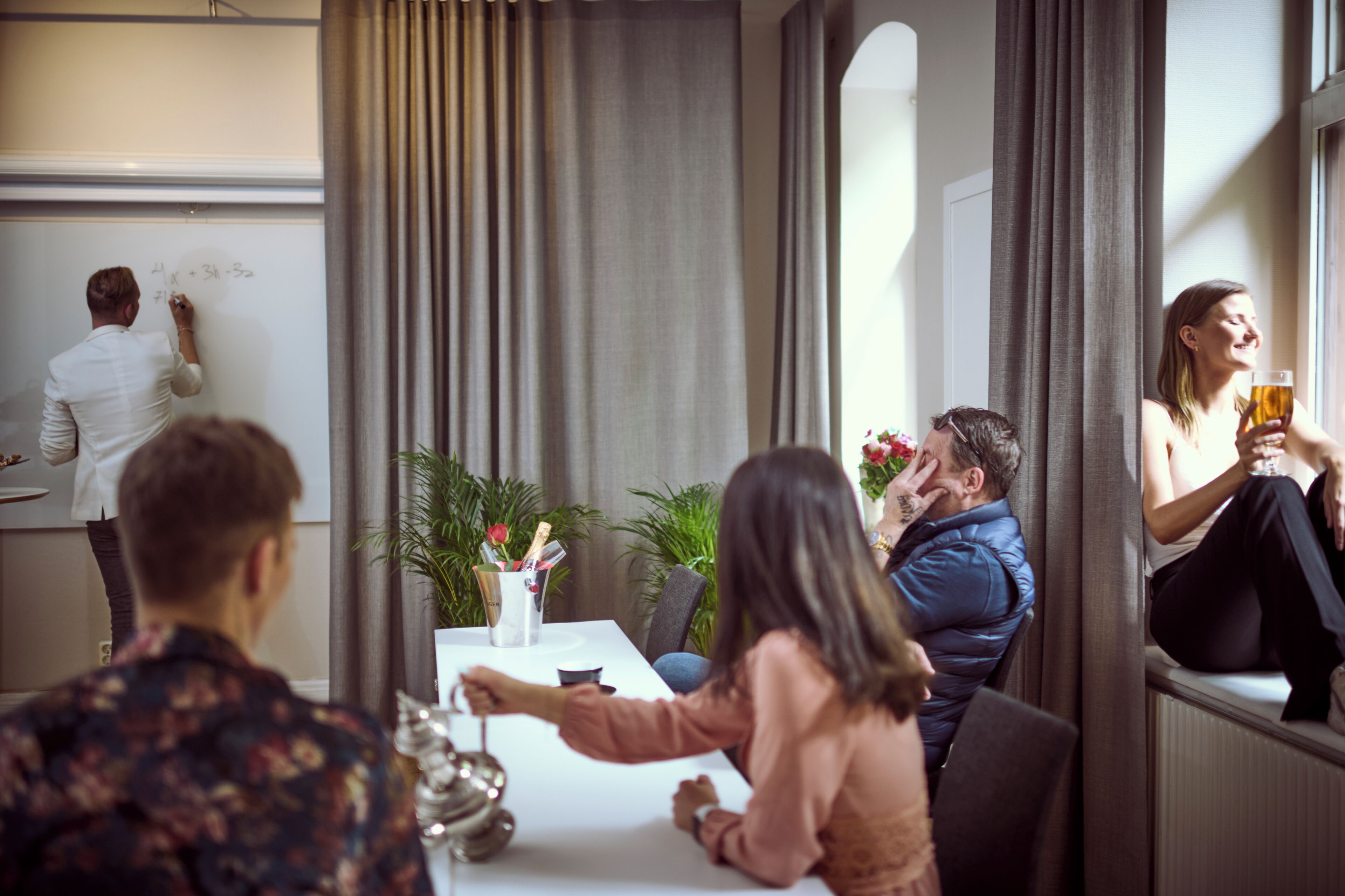 Una sala de reuniones con una pizarra, una mesa con un florero, y un ventanal con cortinas.