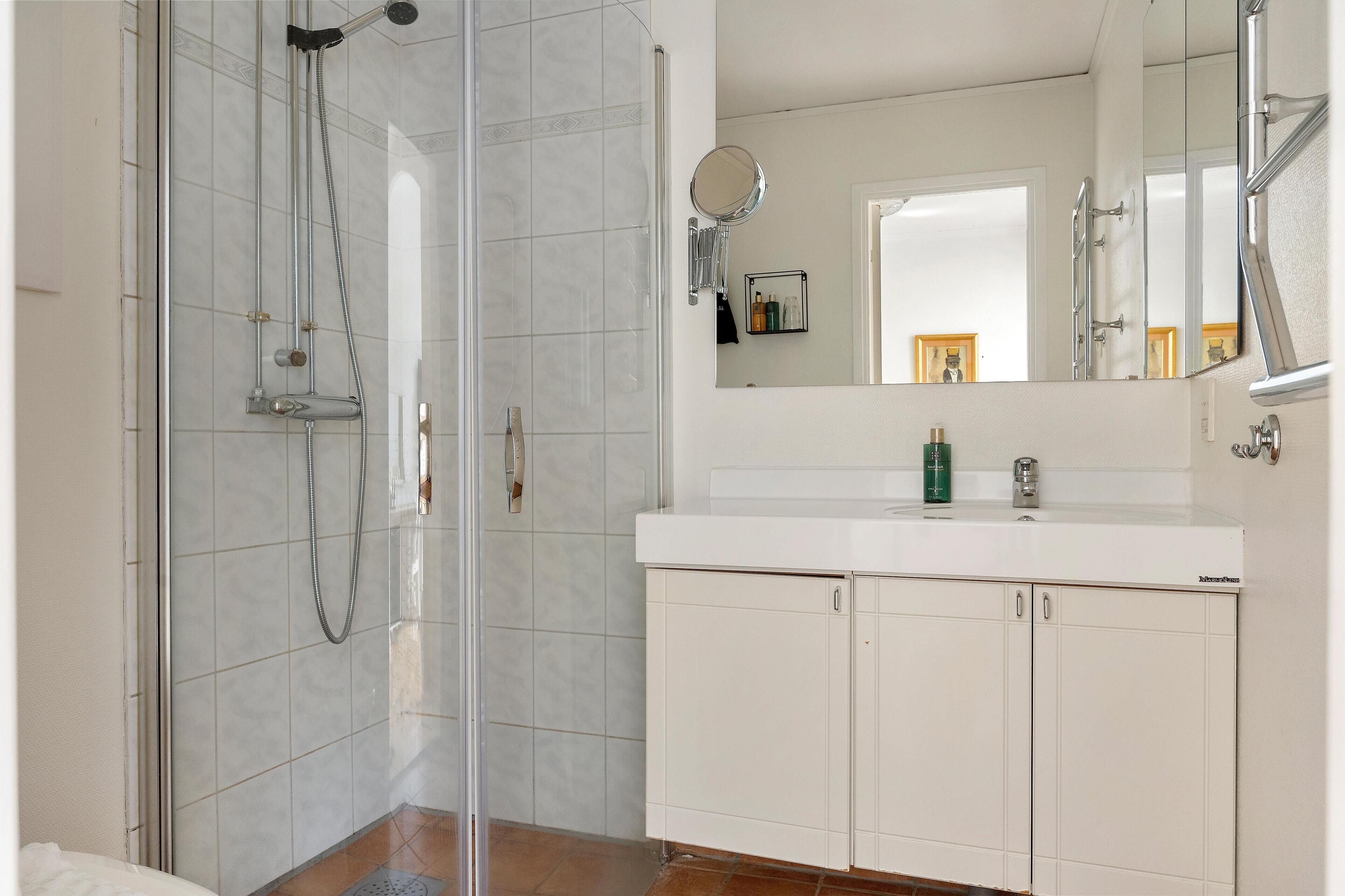 A bathroom with a glass shower enclosure, a white vanity with a mirror, and a tiled floor.