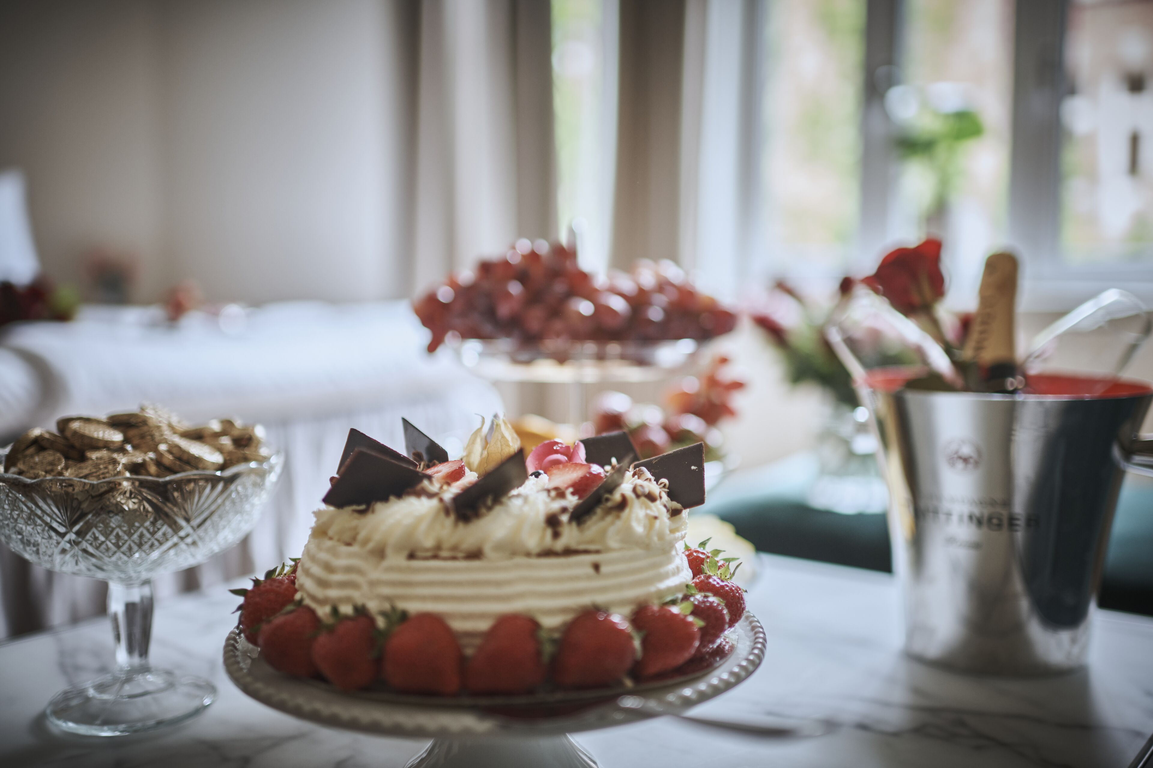 A dessert table with a cake, strawberries, and a glass bowl of cookies.