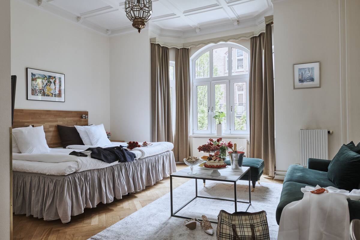 A bedroom with a bed, a coffee table, a sofa, and a large window with curtains.