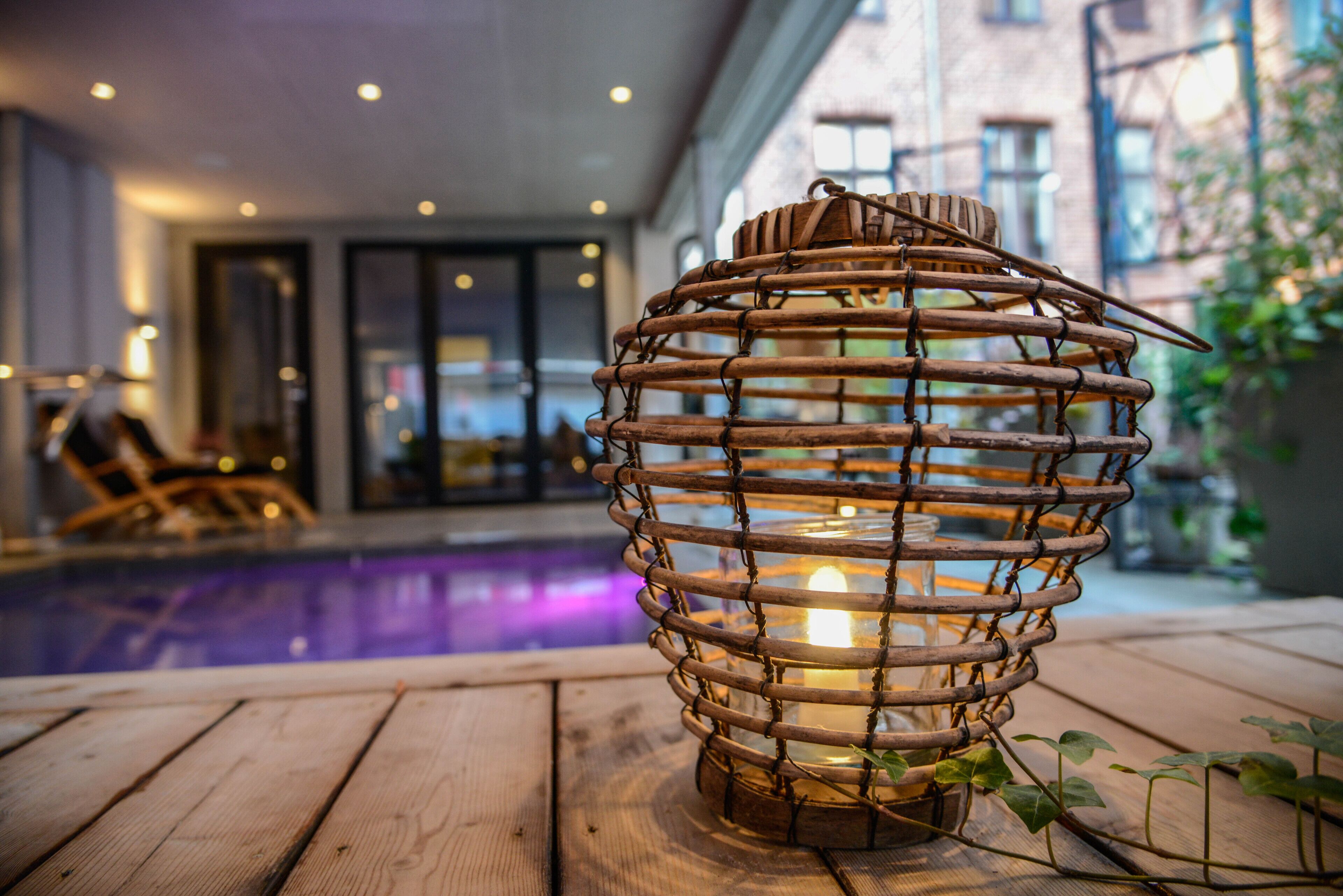A wooden lantern with a candle inside, placed on a wooden deck near a pool.