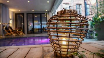 A wooden lantern with a candle inside, placed on a wooden deck near a pool.