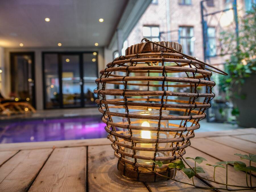 A wooden lantern with a candle inside, placed on a wooden deck near a pool.