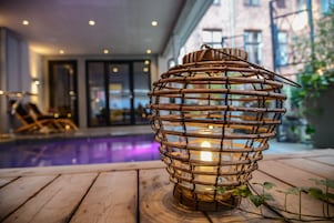 Un farol de madera con una vela en su interior, colocado en una cubierta de madera cerca de una piscina.