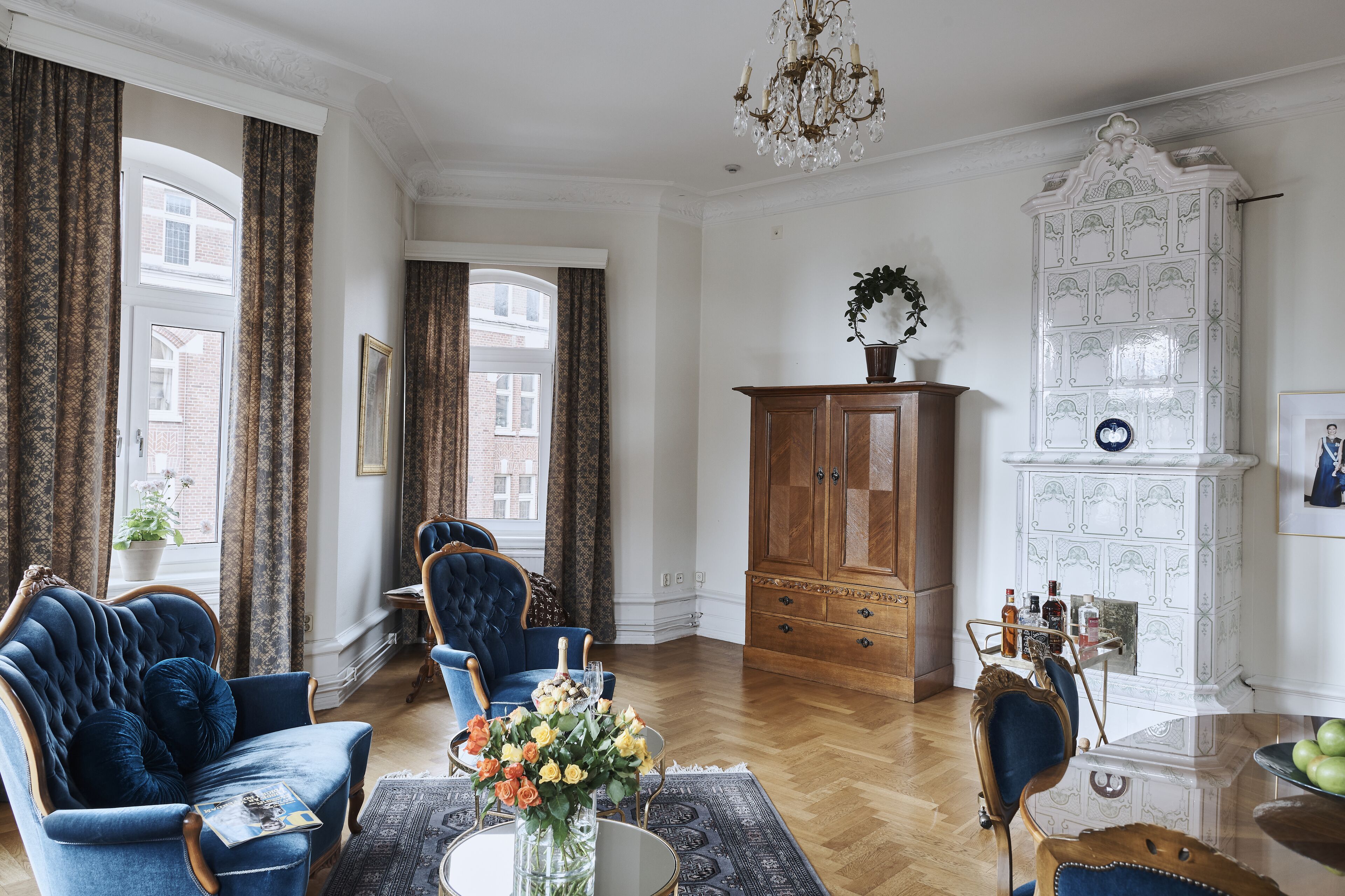 Ein Zimmer mit blauem Sessel, Holzschrank und Kamin mit weißen Fliesen.