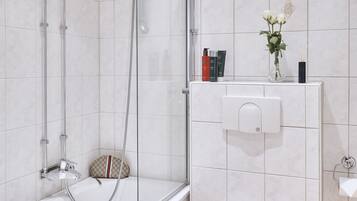 A modern bathroom with a glass-enclosed shower, a white bathtub, and a toilet with a decorative item on top.