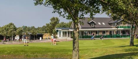 Un campo de golf con club house, un estanque y árboles.