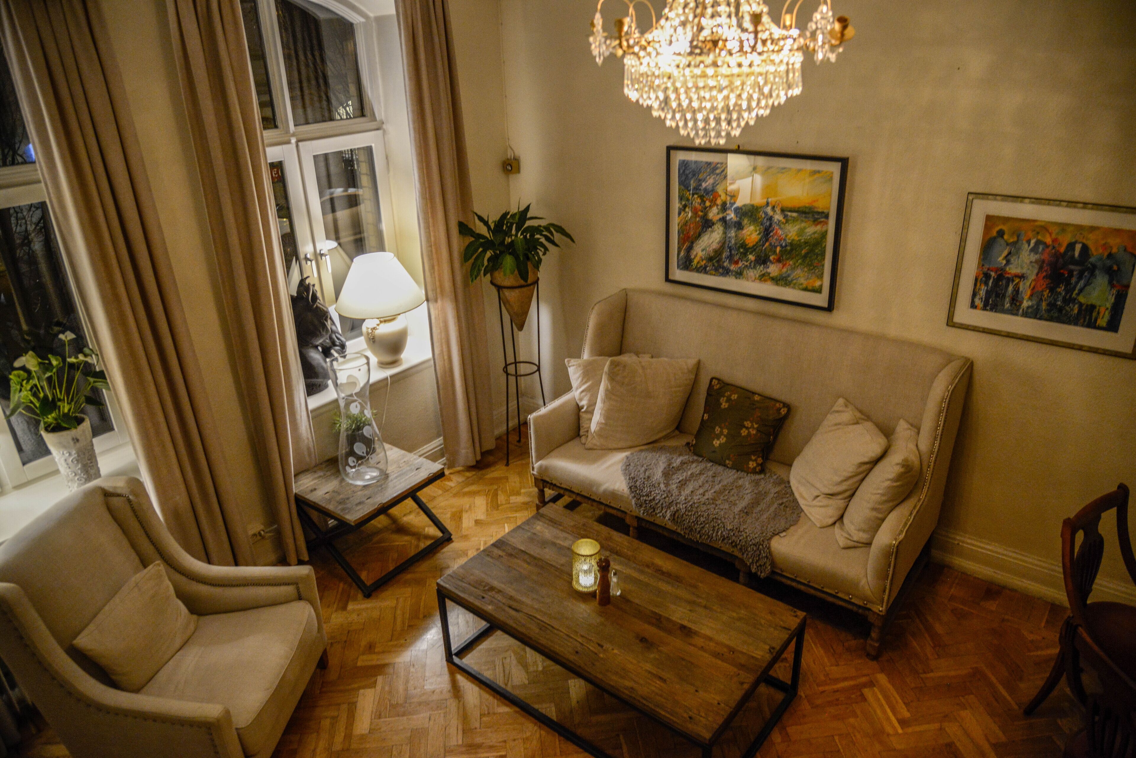 A living room with a sofa, armchair, wooden coffee table, and a chandelier.