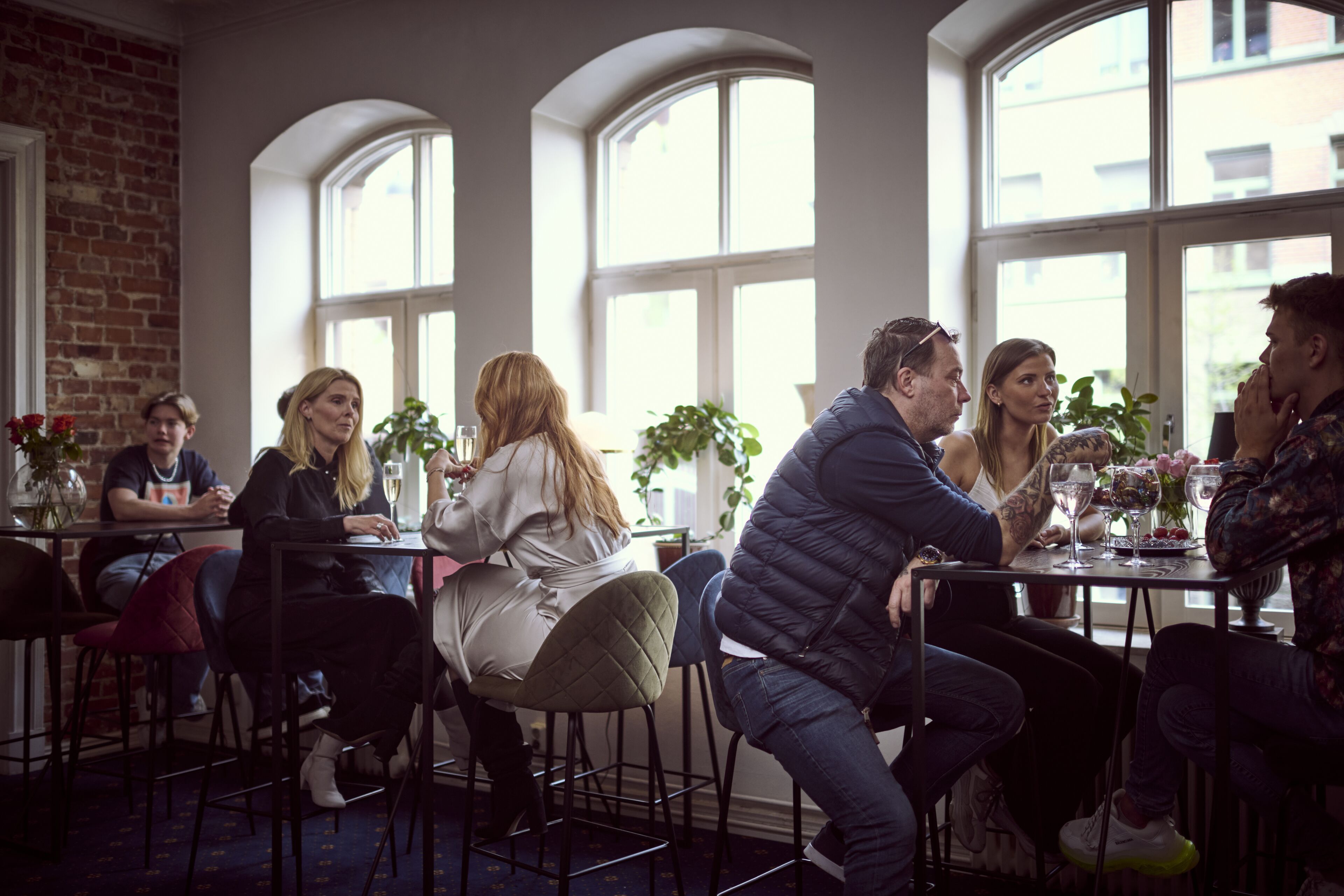 Un grupo de personas sentadas en una mesa en una habitación con ventanas de arco y pared de ladrillo.