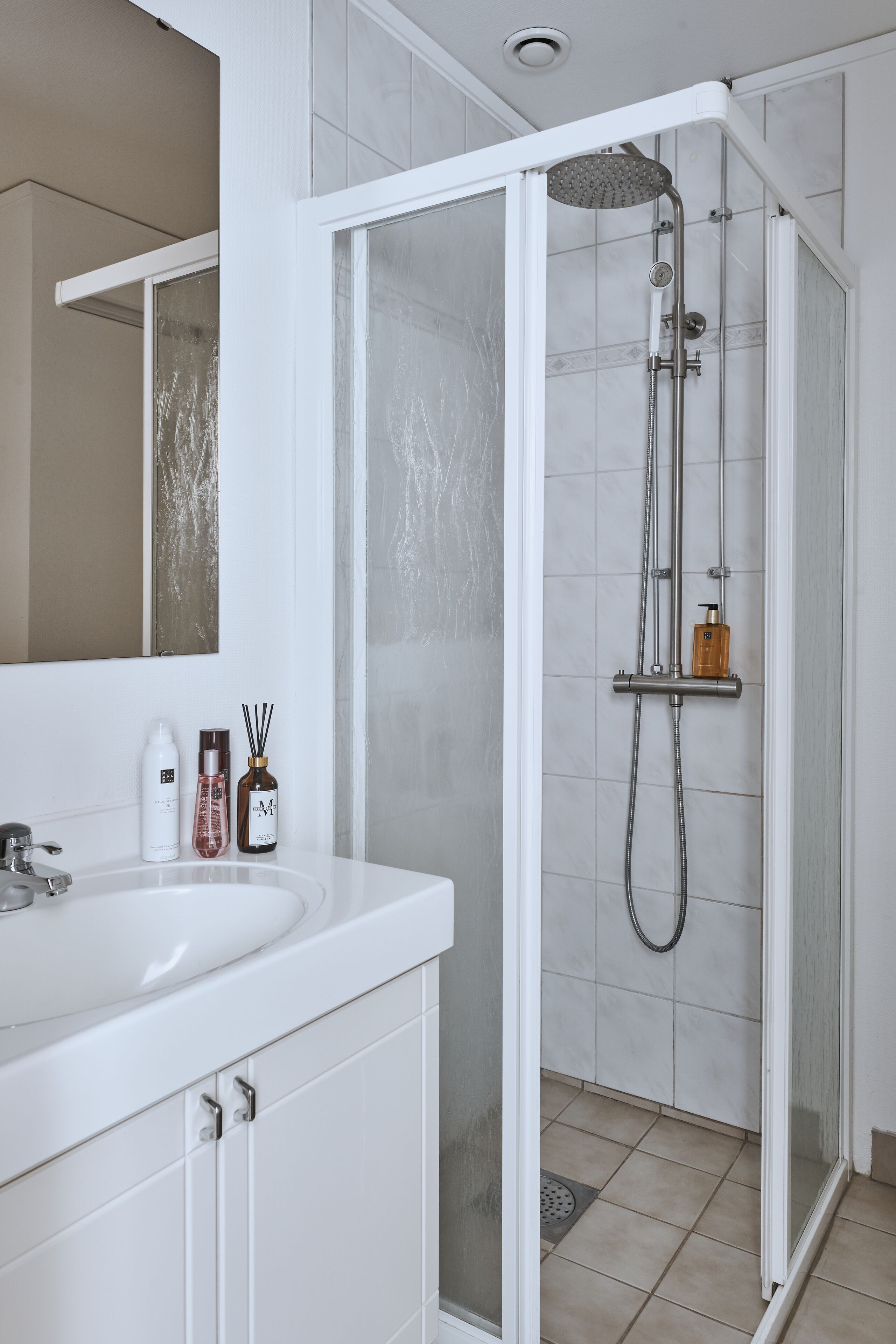 A modern bathroom with a white sink, mirror, and shower enclosure.