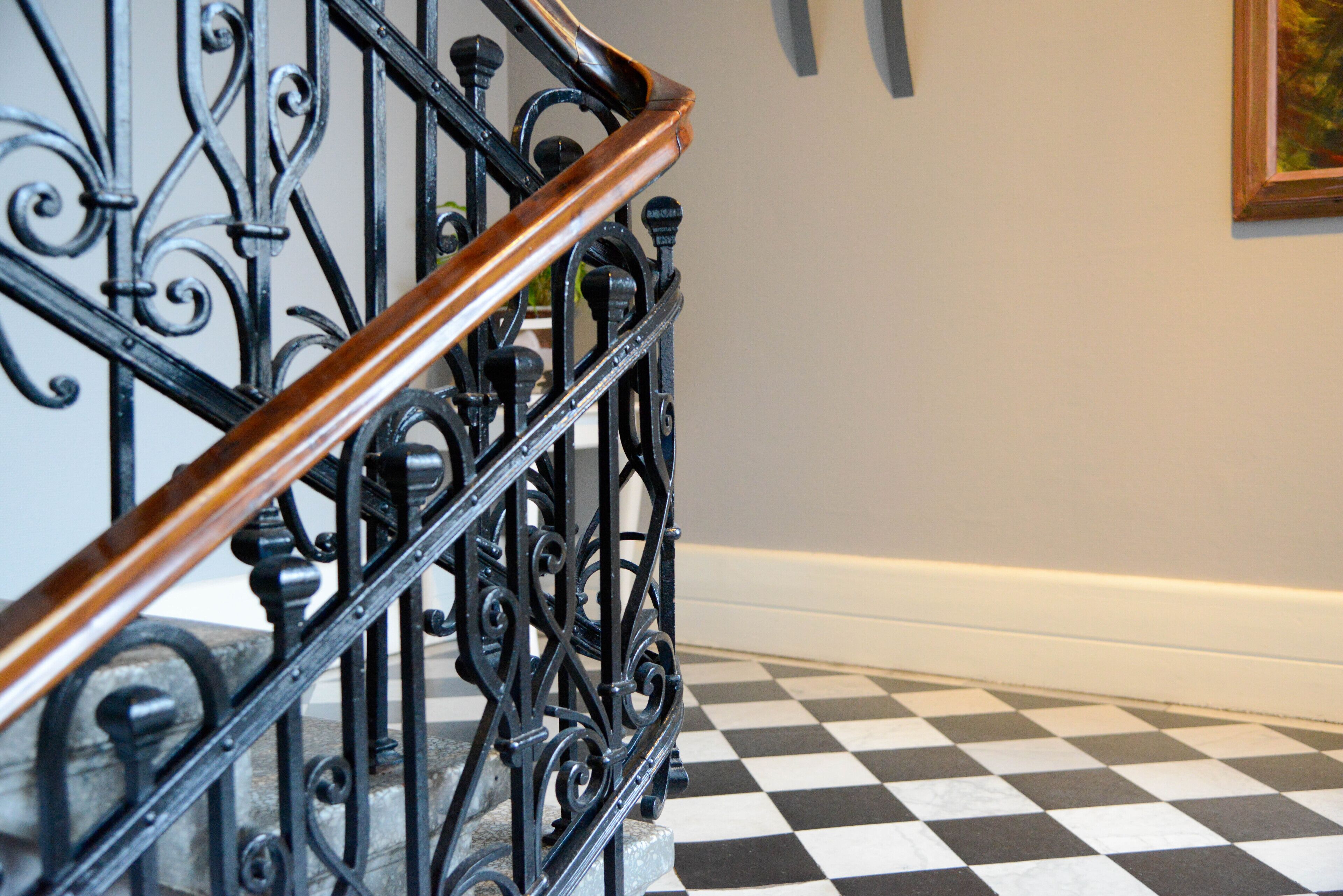 A black and white checkered floor and a wooden handrail on a staircase with ornate black metal railings.