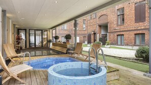 Zona de piscina con sillones de descanso, un jacuzzi y vistas a un edificio de ladrillo.