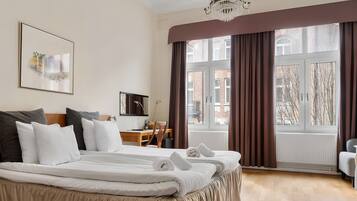 A hotel room with a large bed, a desk, a chair, and a view of the city through large windows.