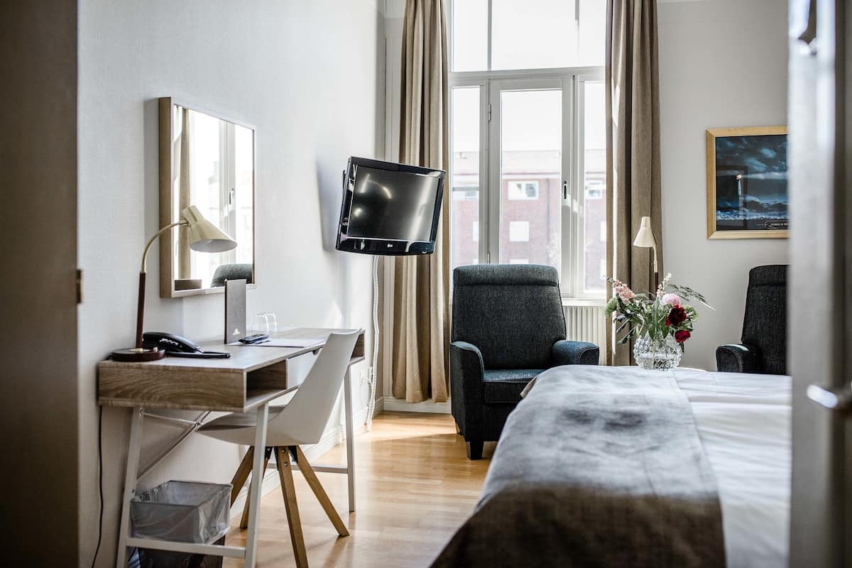 Hotellihuone, jossa on sänky, työpöytä, tuoli, televisio ja ikkuna, jossa on verhot.