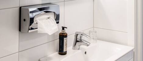 A modern bathroom with a white sink, a hand dryer, a paper towel dispenser, and a mirror.