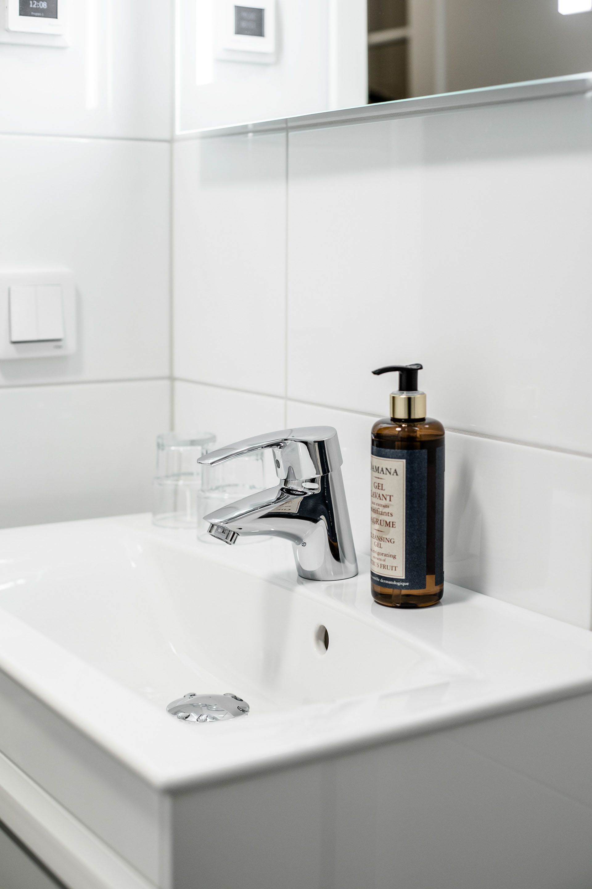 Ein weißes Waschbecken mit chromfarbenem Wasserhahn und einer Gel-Flasche daneben.