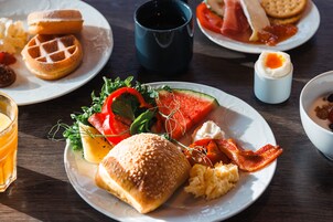 Una mesa de madera con waffles, huevos, tocino y una variedad de frutas y verduras para el desayuno.