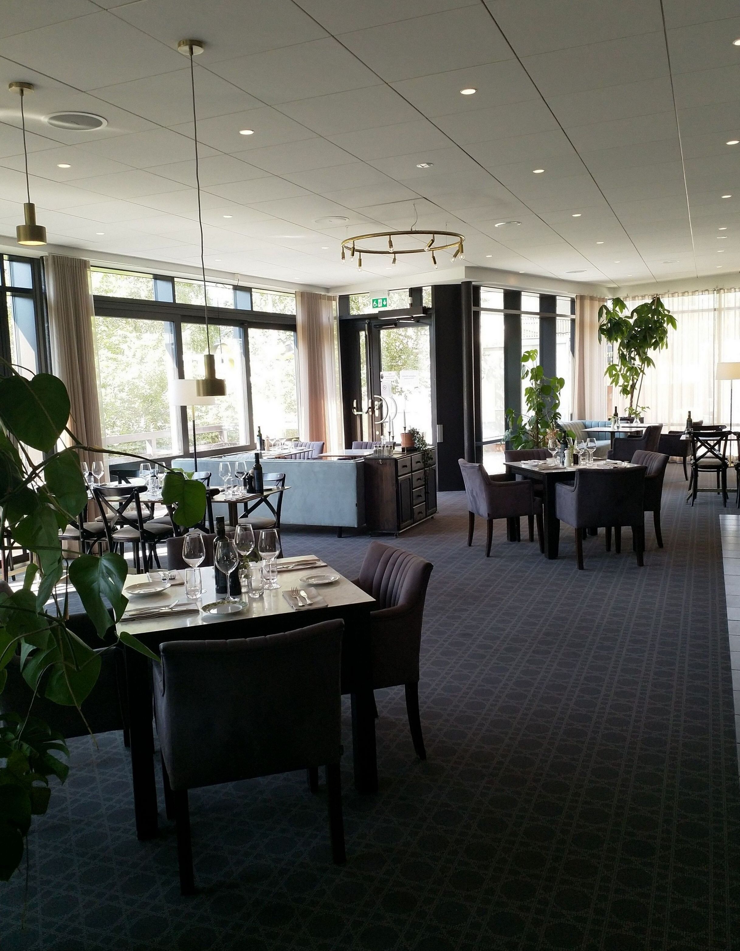 A spacious dining area with tables set for dining, large windows allowing natural light, and a modern ceiling design.