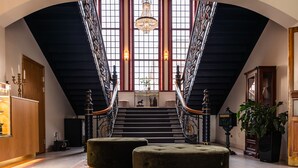 Un magnifique escalier orné de balustrades travaillées, un lustre et une grande fenêtre donnant sur l’intérieur.
