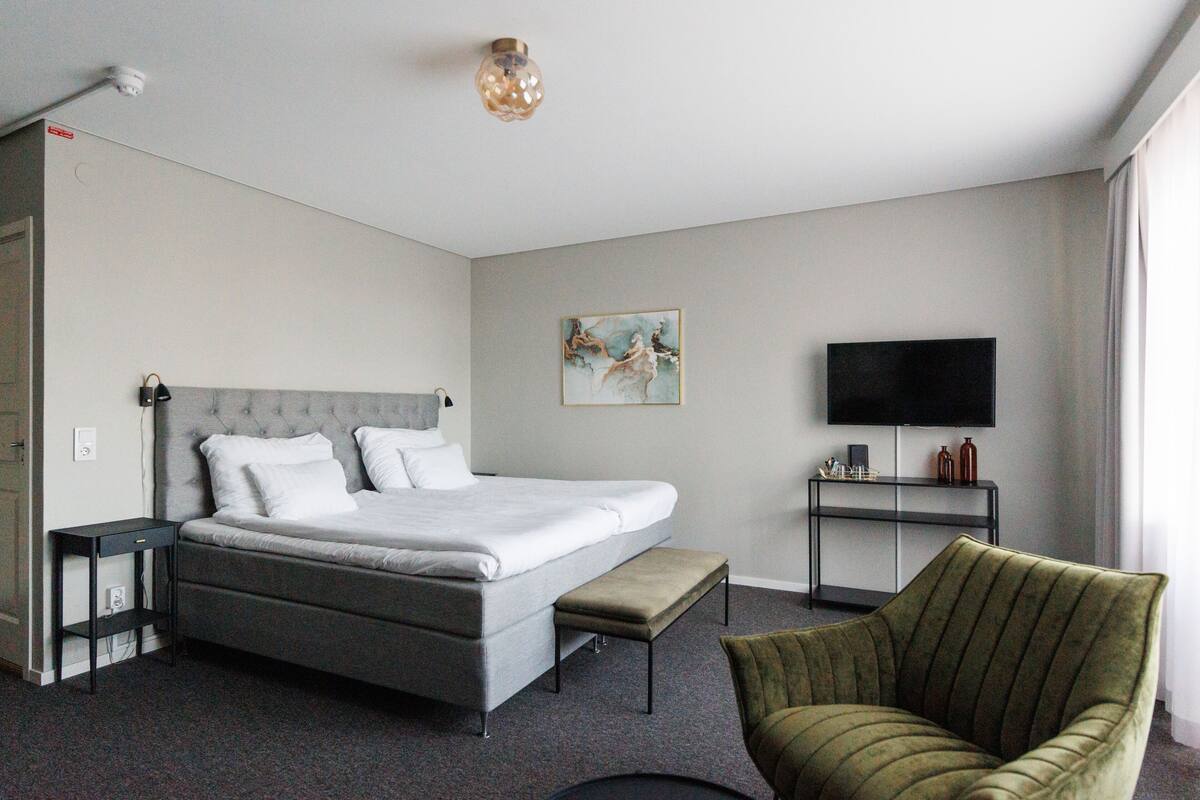 Hotellihuone, jossa on sänky, televisio, tuoli ja taulu seinällä.