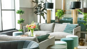 A modern living room with a sectional sofa, round ottomans, and a coffee table. There are potted plants and a floor lamp. - Scandic Stora Hotellet (Nykoping)