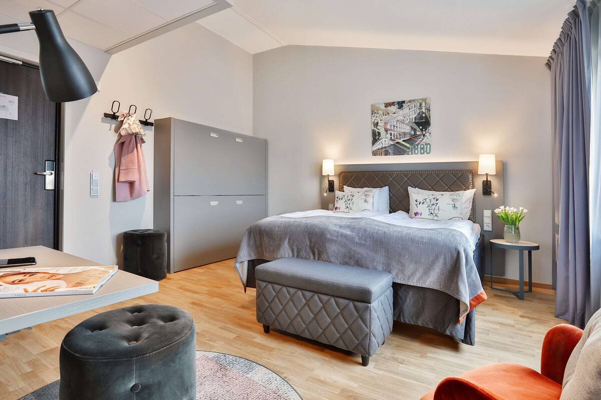 A modern hotel room with a bed, bedside tables, a desk, and a chair.