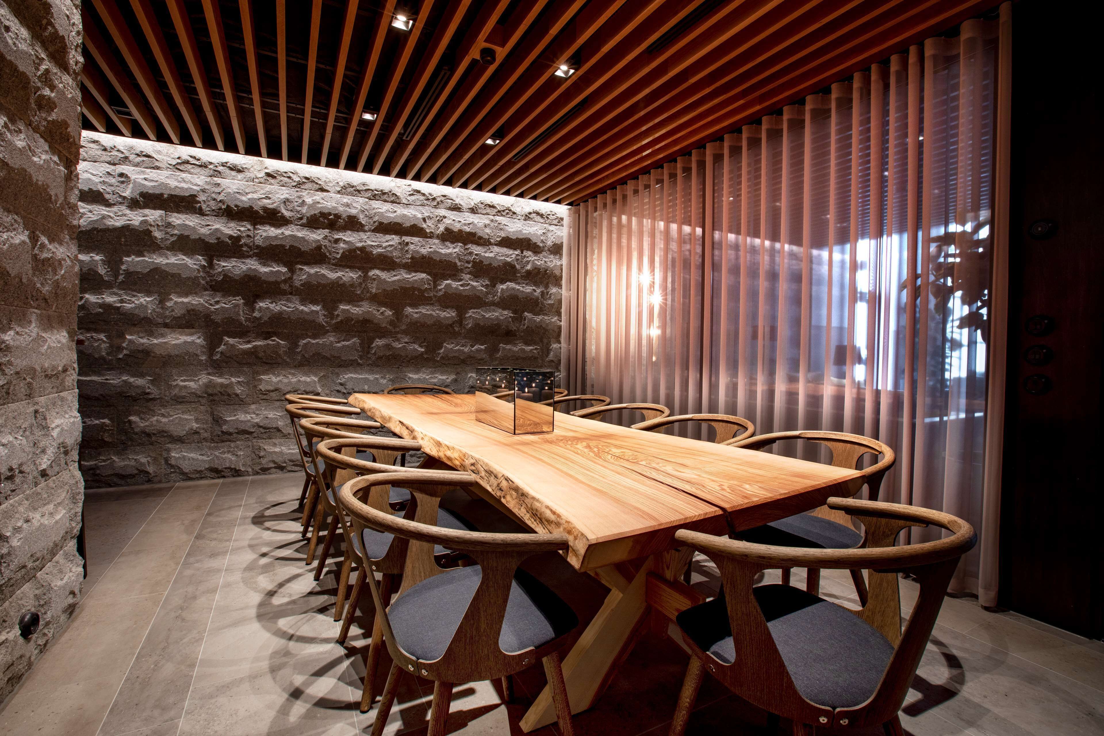 Una sala de conferencias con una mesa y sillas de madera, paredes de piedra y un techo moderno.