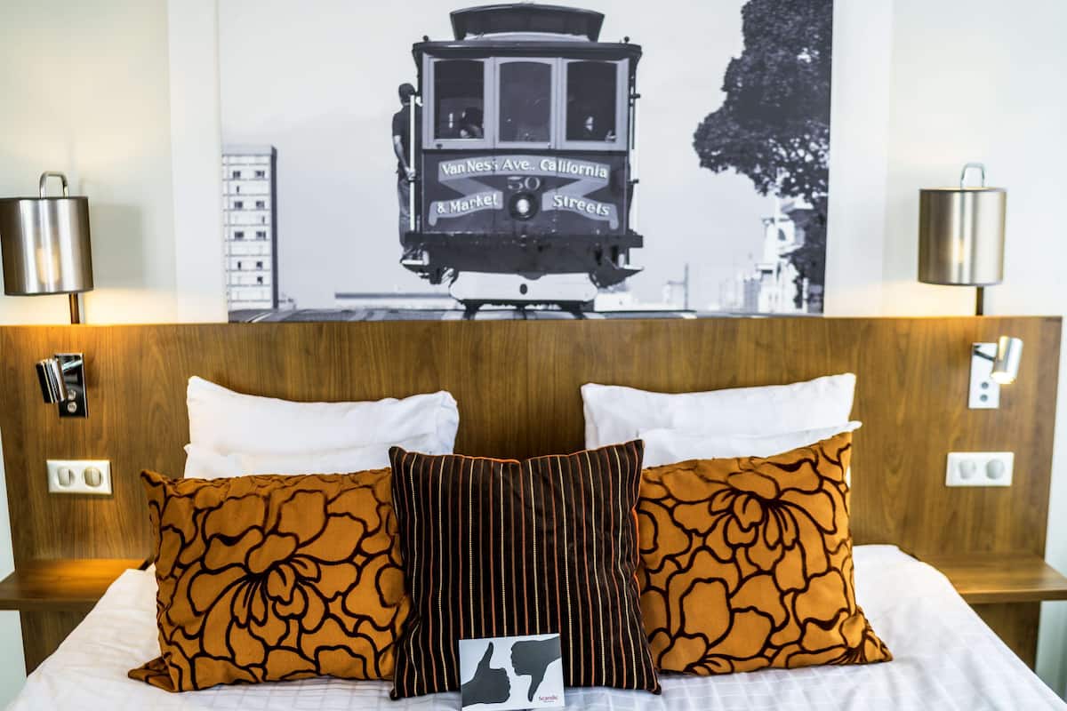 A hotel room with a bed, two pillows, a headboard, and a wall-mounted picture of a trolley.