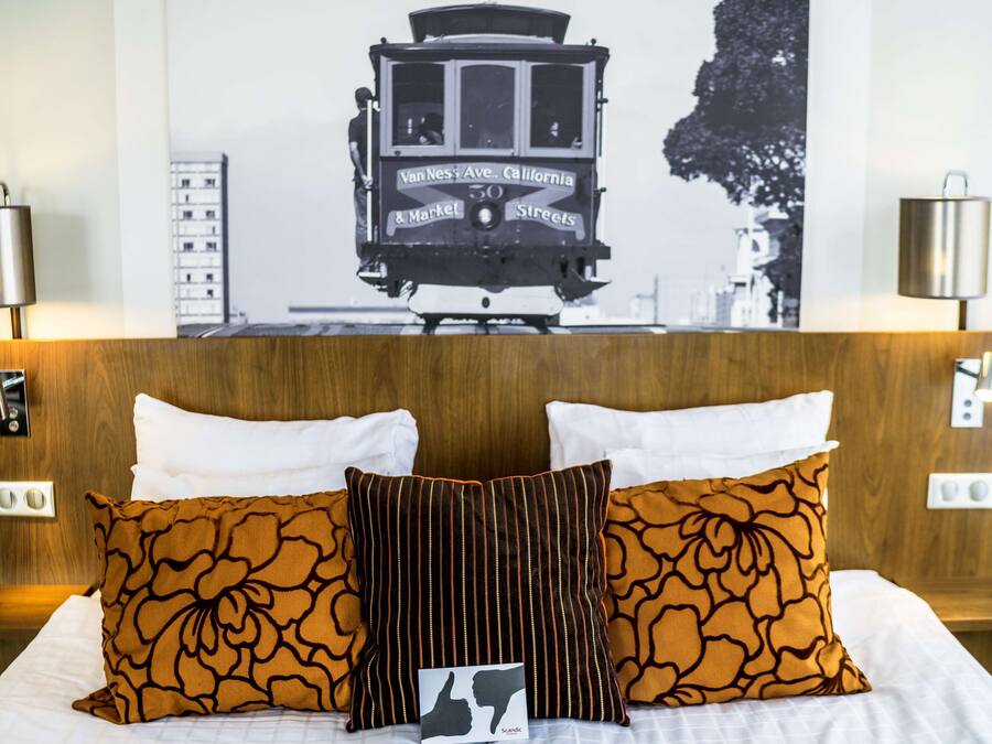 A hotel room with a bed, two pillows, a headboard, and a wall-mounted picture of a trolley.
