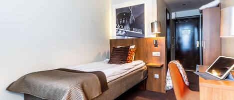 Quarto de hotel com uma cama, uma escrivaninha com um laptop, uma cadeira e uma luminária na parede.