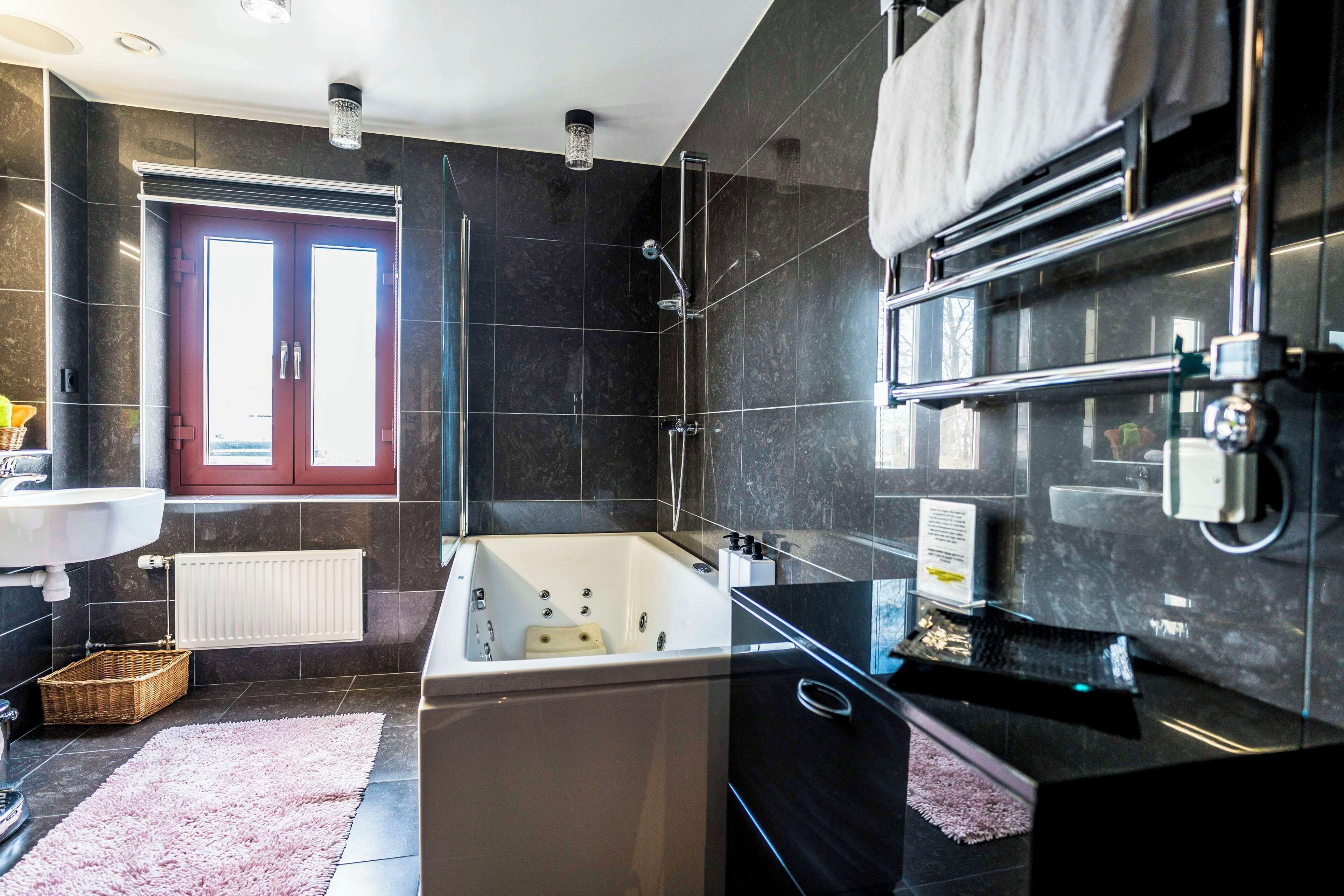 A modern bathroom with a large bathtub, a glass shower enclosure, a sink, and a red-framed window.