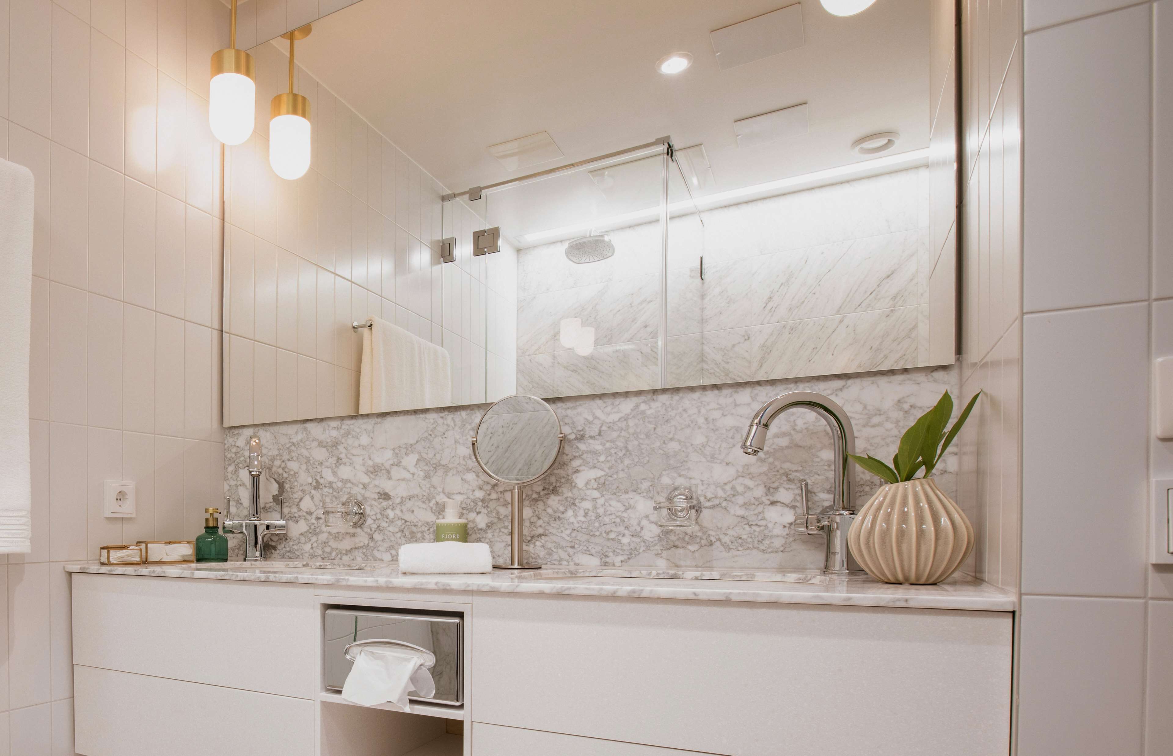 Une salle de bain moderne avec un lavabo en marbre, un miroir rond, une douchette à main et une plante en pot.