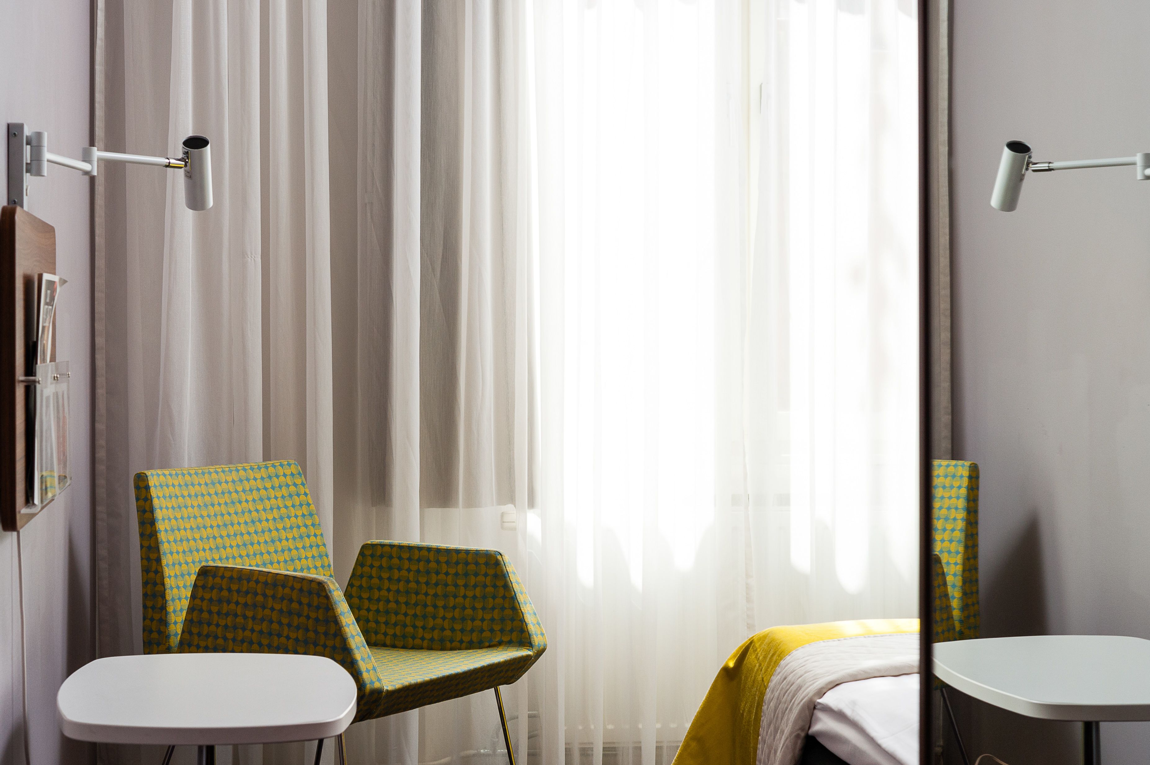 Una habitación de hotel con una cama, dos sillas, una mesita y un espejo.