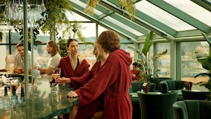 A modern bar area with a glass ceiling, green chairs, and a view of the cityscape.