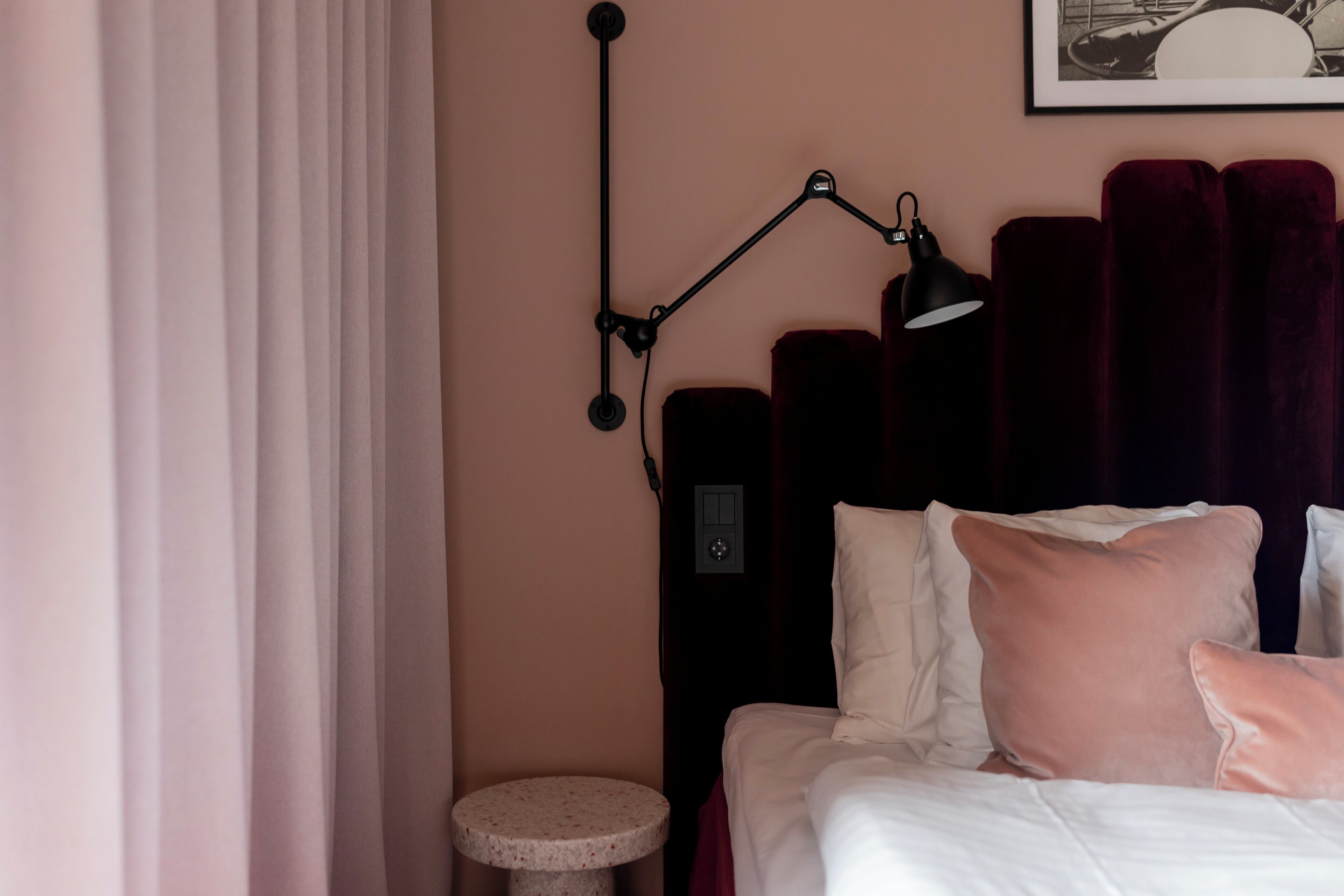 A neatly made bed with pillows, a bedside lamp, a small round table, and a wall-mounted light fixture.