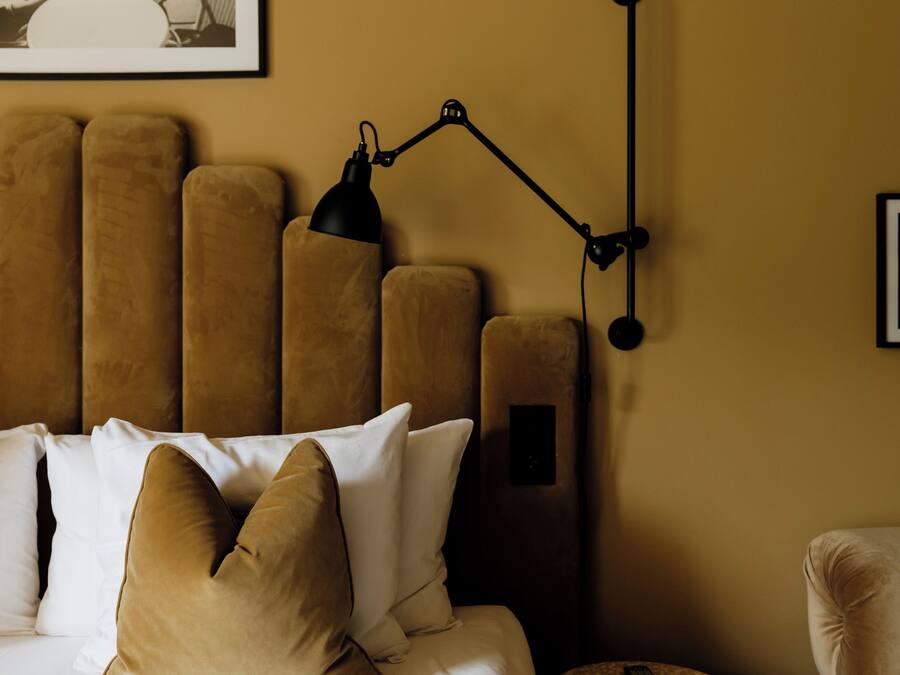 Un dormitorio con cama, almohadas, cabecera, lámpara y un cuadro en la pared.
