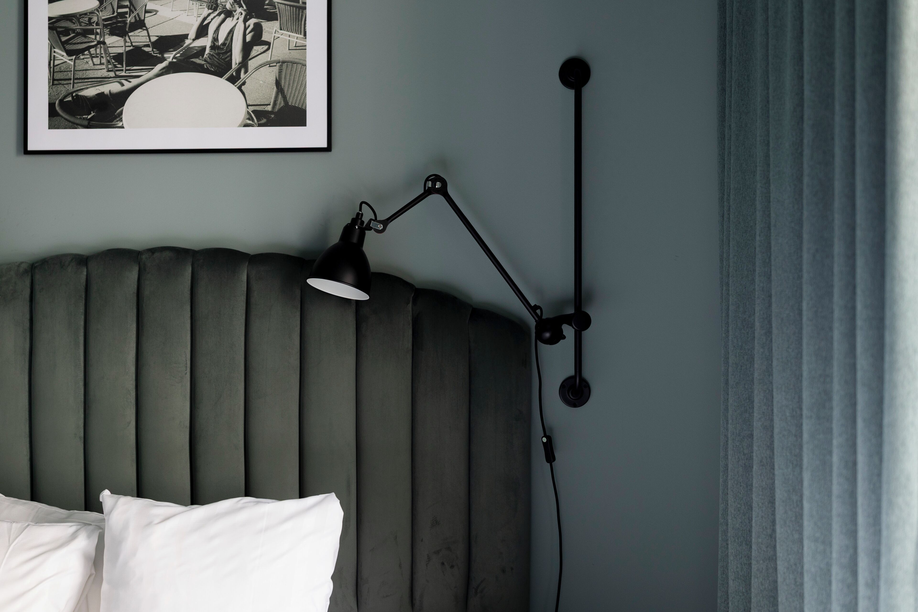 A bed with a headboard, a black desk lamp, and a framed picture on the wall.