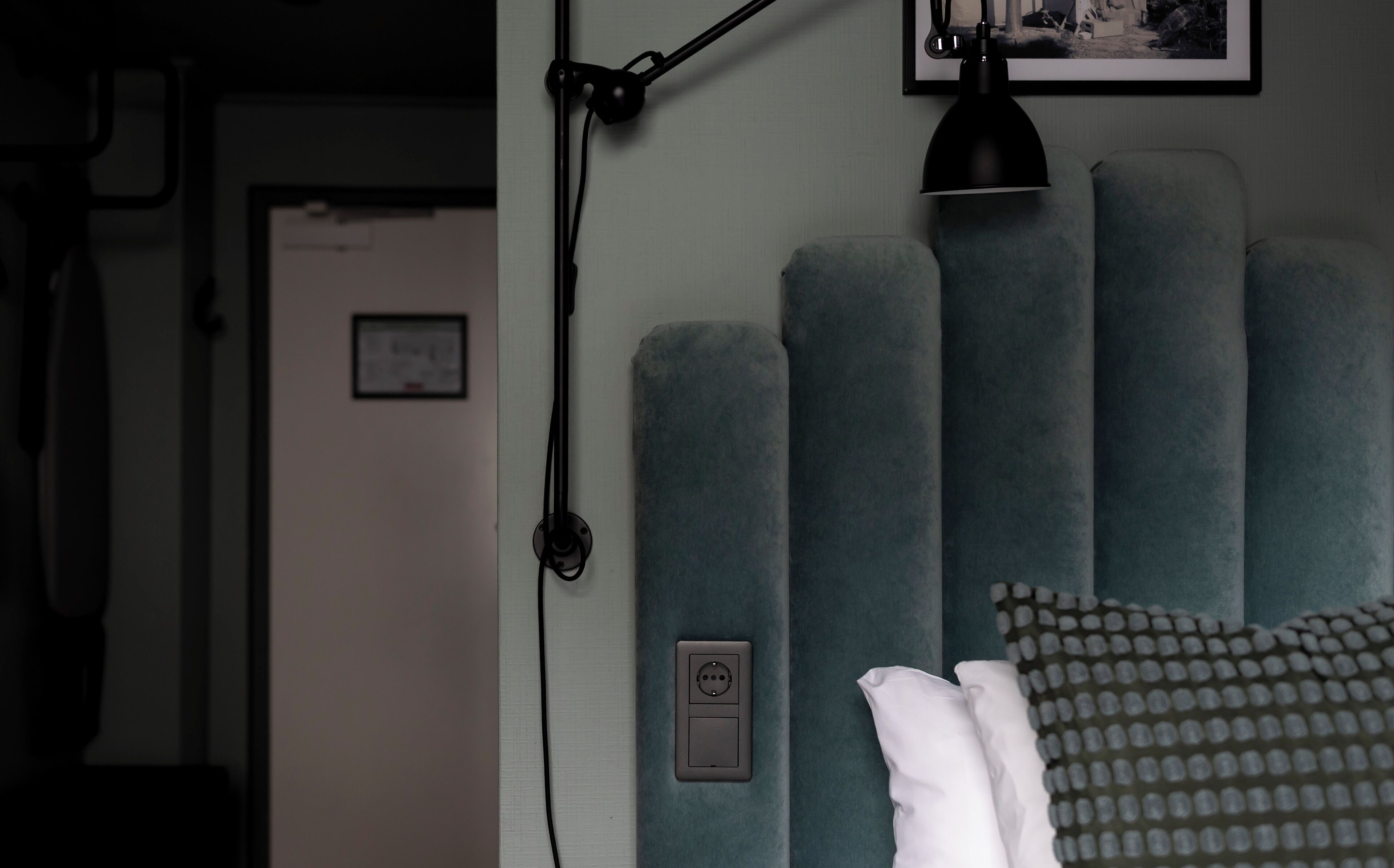 Une chambre avec un lit, une prise de courant fixée au mur et un tableau encadré.