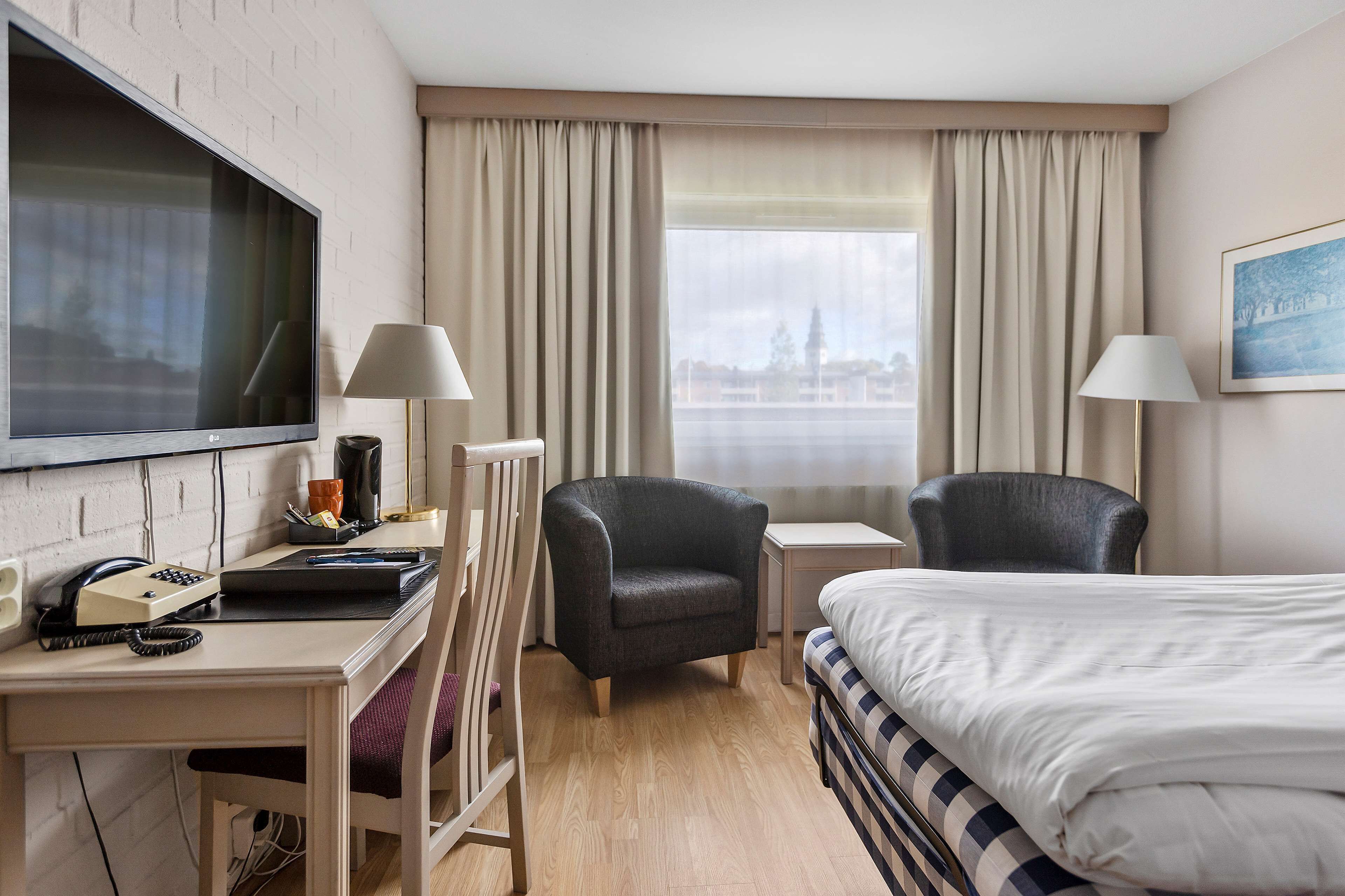A hotel room with a bed, desk, chair, TV, and a window with curtains.