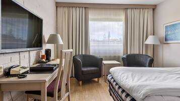A hotel room with a bed, desk, chair, TV, and a window with curtains.