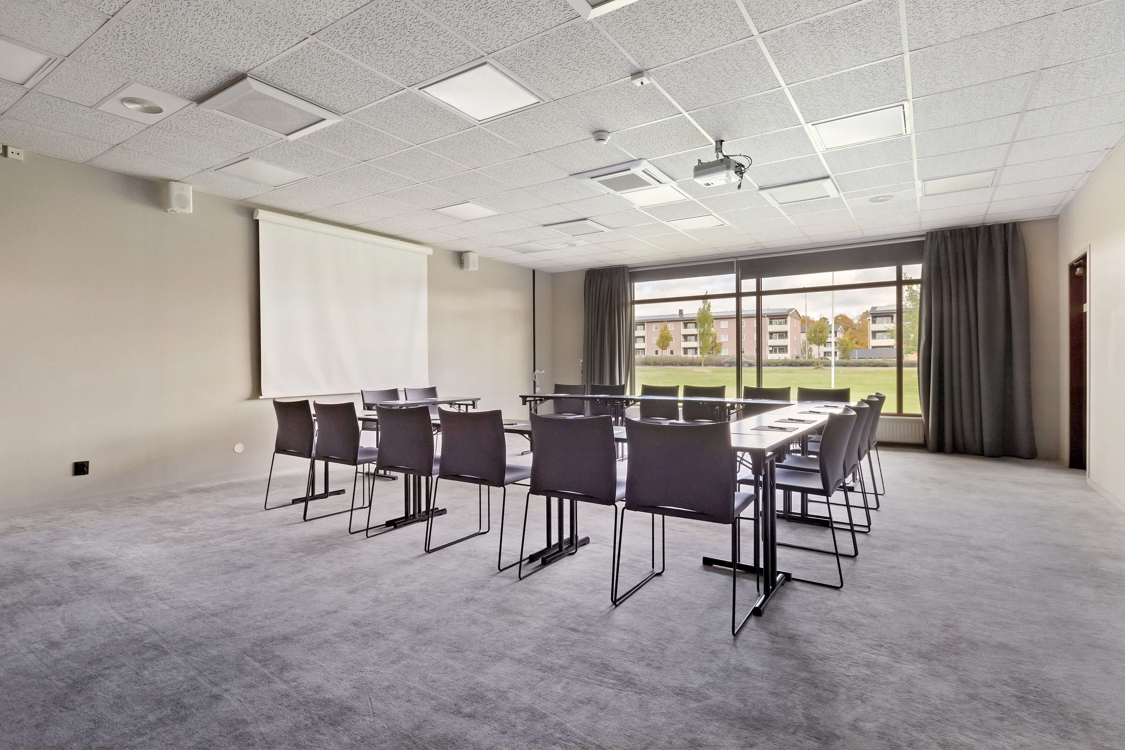 A conference room with a large table, chairs, a projector, a screen, and a view of buildings through large windows.