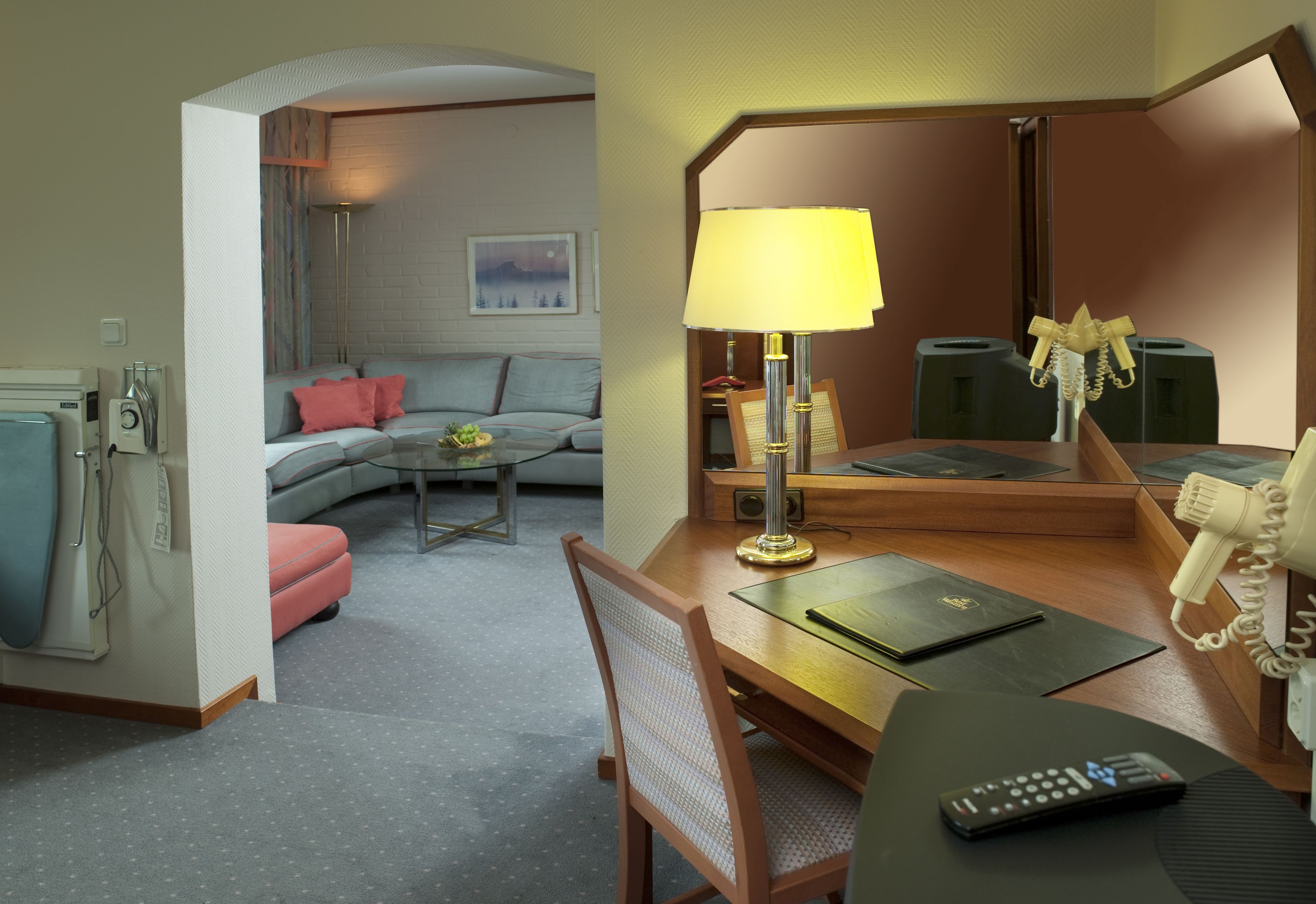 Habitación de hotel con sofá, una mesita, escritorio con lámpara, teléfono y una silla.