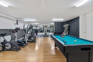 Un gimnasio con bicicletas estáticas, mesa de billar y un espejo.
