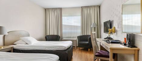 A hotel room with two beds, a desk, a chair, a TV, and a window with curtains.