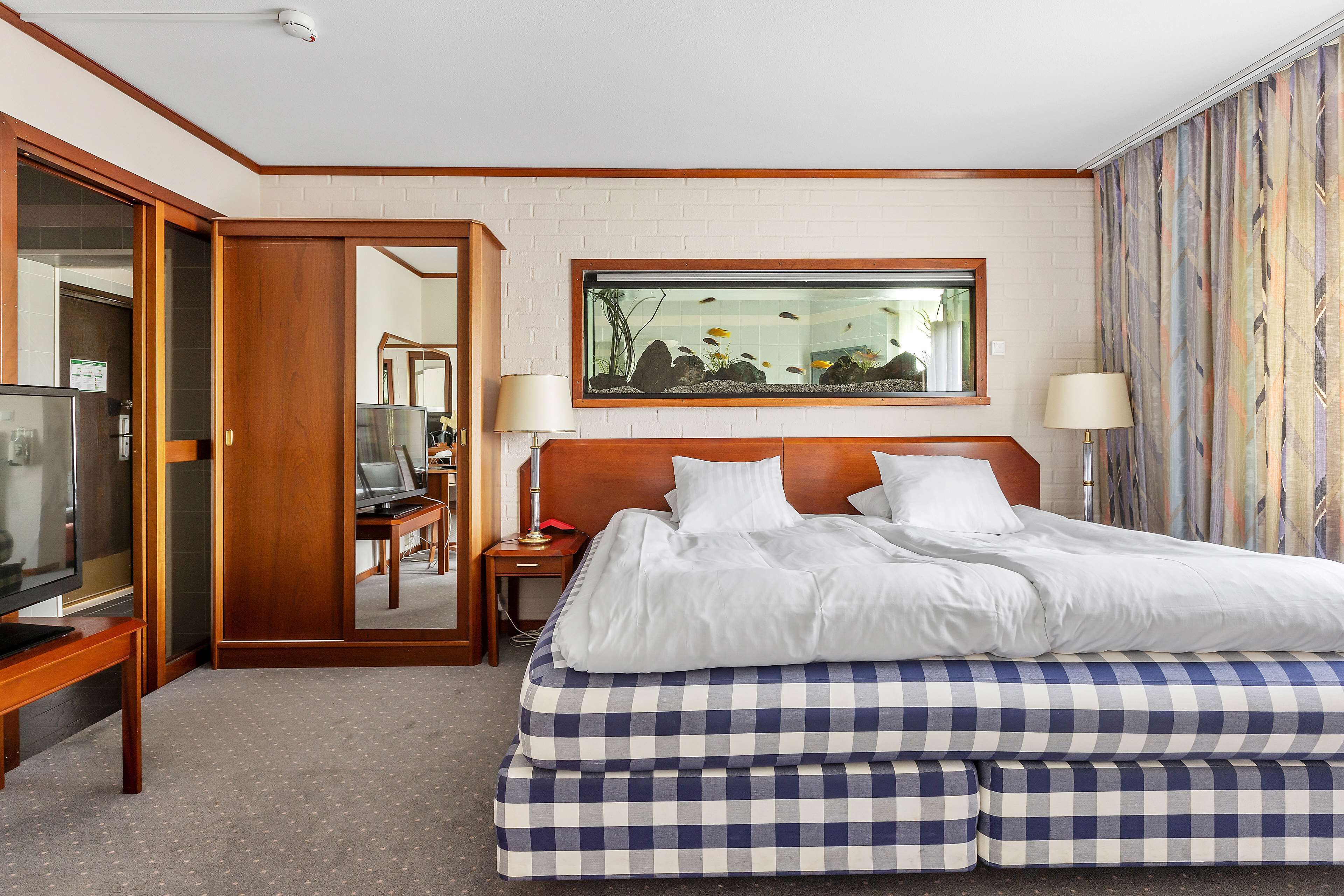 Habitación de hotel con una cama grande, televisor, escritorio con lámpara y un cuadro en la pared.