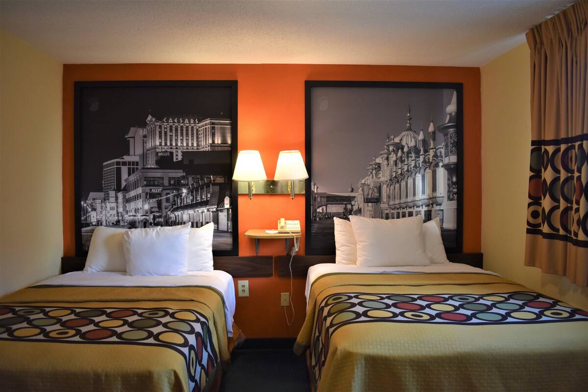 A hotel room with two beds, a nightstand, and two wall-mounted lamps.