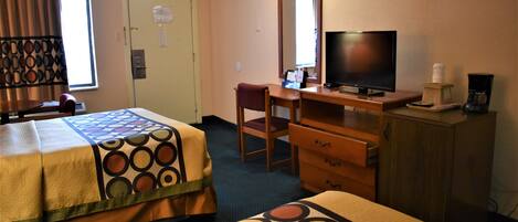 A hotel room with two beds, a desk with a television, a chair, a dresser, and a coffee maker.